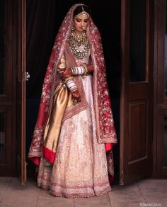 a woman in a white and gold bridal gown standing at the entrance to her home