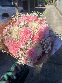 a bouquet of pink and white flowers is held by someone's hand on the sidewalk