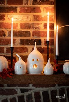 some candles are sitting on a mantle in front of a brick wall with pumpkins