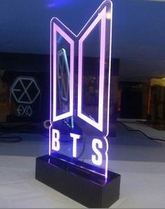 the bts logo is lit up in purple and blue lights on a black stand