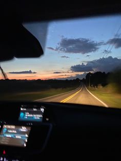 the dashboard of a car on a highway at dusk with clouds in the sky above