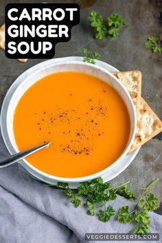 carrot ginger soup in a white bowl with crackers and parsley on the side