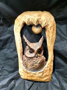 an owl figurine sitting on top of a piece of wood with a ball in it's mouth