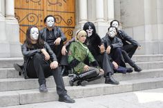 group of people with painted faces sitting on steps in front of an old building wearing masks