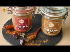 two jars filled with different types of spices on top of a black tray next to each other