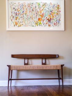 a wooden bench sitting in front of a painting on the wall