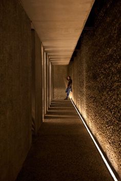 a person walking down a long hallway with lights on either side of the walkway and between two walls