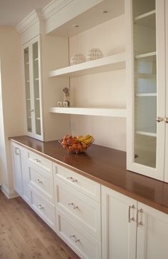 a bowl of fruit sitting on top of a wooden counter next to white cupboards