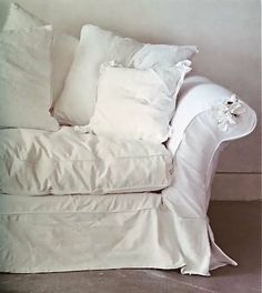 a white couch with many pillows on it's back and side, in front of a wall