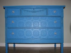 a blue dresser sitting on top of a tile floor next to a wall with a clock