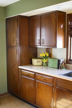 an empty kitchen with wooden cabinets and white counter tops, flowers in a vase on the sink