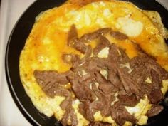 an omelet with meat and cheese is on a black plate, ready to be eaten