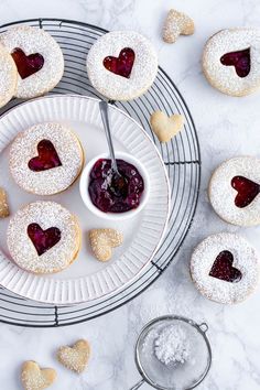 strawberry jam cookies with powdered sugar and heart shaped jelly on top, sitting on a plate