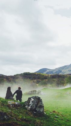 two people sitting on rocks in the middle of a field with steam rising from them