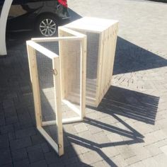 two wooden boxes sitting next to each other on a brick sidewalk near a parked car