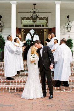 a newly married couple kissing in front of their wedding party at the entrance of a church