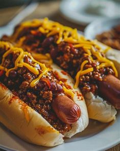 two chili dogs with cheese on them sitting on a plate