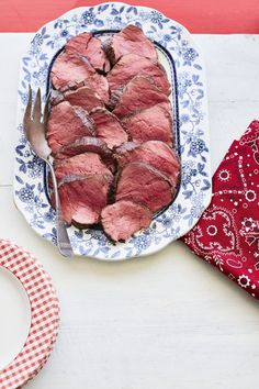 a plate with meat on it next to a red and white napkin