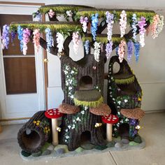 a tree house made out of fake flowers and trees with mushrooms on the roof, in front of a door