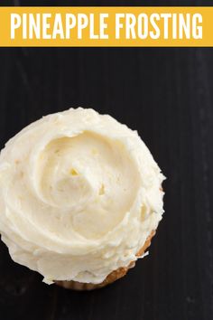 a cupcake with white frosting sitting on top of a black table next to a yellow sign that says pineapple frosting