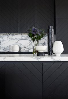 a marble counter top with vases and flowers on it in front of a black wall