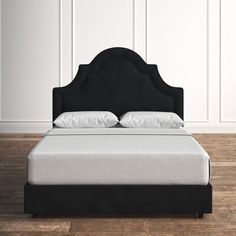 a black bed with white sheets and pillows in a room that has wood floors, walls and wooden flooring