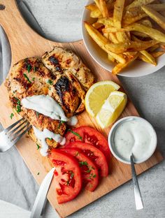 a chicken burger with fries and tomatoes on a cutting board