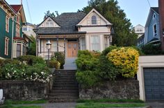 the house is painted green and white with flowers on the front yard, along with several other houses