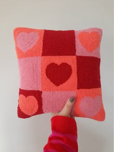 a hand holding up a pillow with hearts on the front and back, which are red and pink