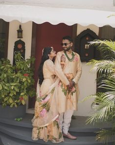 a man and woman standing on the steps in front of a building with plants around them