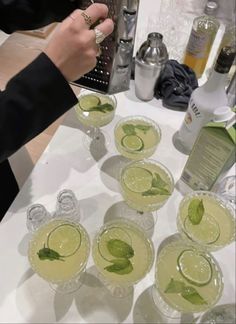 several glasses filled with green drinks on top of a white table next to bottles and silverware