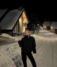 a woman standing in the snow with her arms spread out and lights on behind her