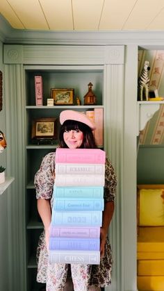 a woman holding stacks of books in front of her face while standing next to a bookcase