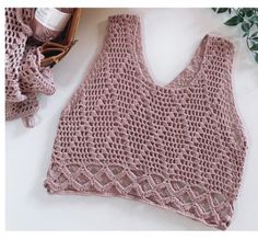 a pink crocheted tank top next to some knitting supplies and a green plant