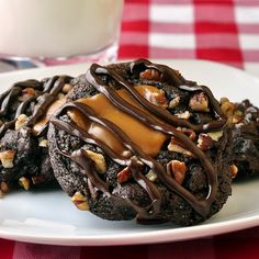 two chocolate cookies with nuts and caramel drizzled on top sitting on a white plate