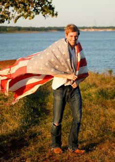 a man holding an american flag in front of the water with his arms wrapped around him