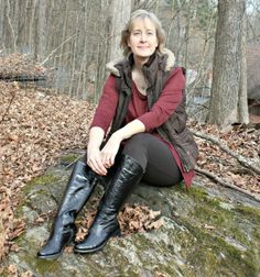 a woman sitting on top of a rock in the woods with her legs crossed and wearing black boots