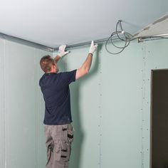 a man is working on the ceiling in his room with wires attached to the wall