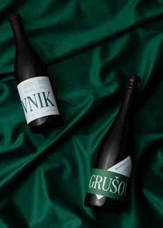 two bottles of wine sitting on top of a green satin covered tablecloth with the names gruso and winkk