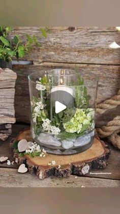 a glass vase filled with flowers and rocks on top of a wooden table next to a rope