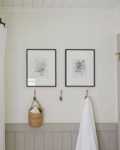 two framed pictures hang on the wall above a towel rack