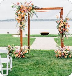 an outdoor ceremony setup with flowers and greenery on the grass by the water in front of it