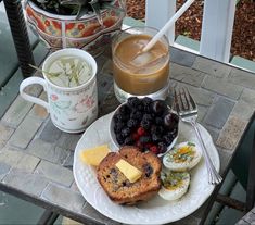 a breakfast plate with toast, fruit and coffee on a patio table next to potted plants