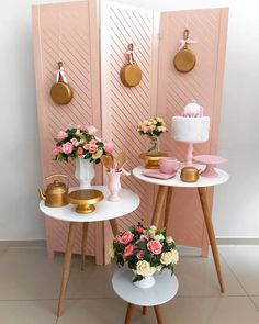 two small tables with flowers on them in front of a pink wall and gold plates