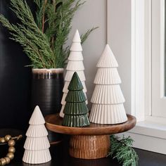 three ceramic christmas trees sitting on top of a wooden tray next to a potted plant