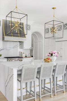 a white kitchen with marble counter tops and gold chandelier hanging from the ceiling