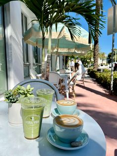 two cups of coffee sitting on top of a table next to each other near palm trees