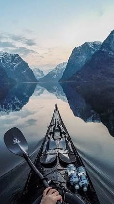 a person in a kayak paddles through the water with mountains in the background