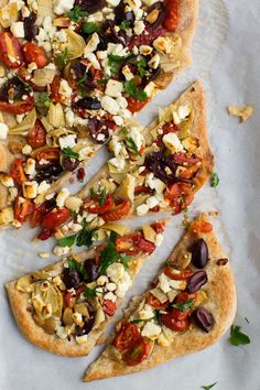 a pizza with olives, tomatoes, and other toppings on top of parchment paper