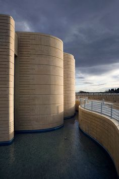 an unusual building with curved walls next to a body of water under a cloudy sky